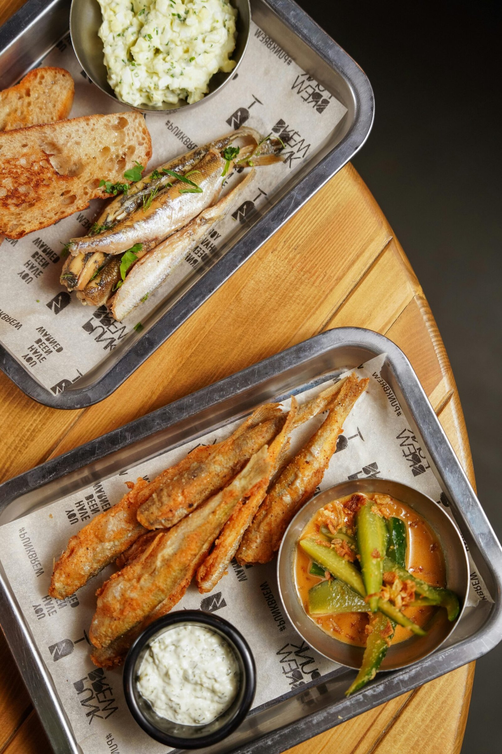 Top view of gourmet fried fish served with dips and bread on a metallic tray, ready for a delicious meal.