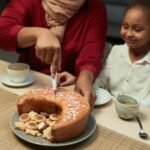 A mother slicing a cake with her daughter at a dining table, creating warm family moments.